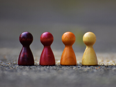 Four wooden game pawns in dark red, red, orange and yellow standing in a row on stone