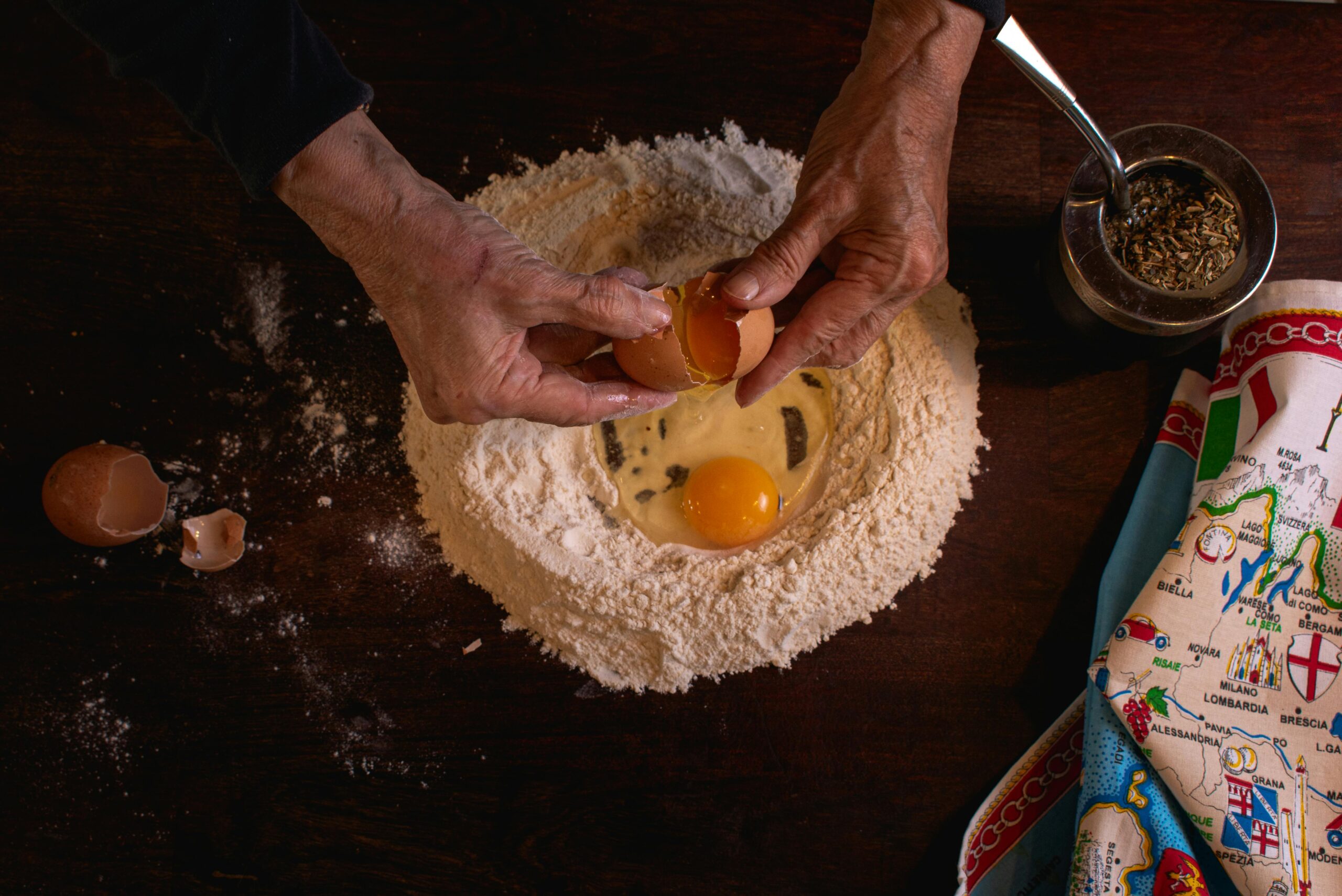 Senior adult cracking an egg into flour for pasta in a home kitchen